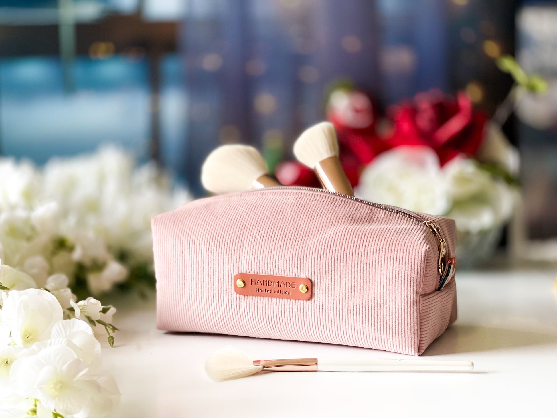 Pink cosmetic bag with a brand logo on a blurred floral background