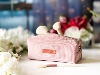 Pink cosmetic bag with a brand logo on a blurred floral background