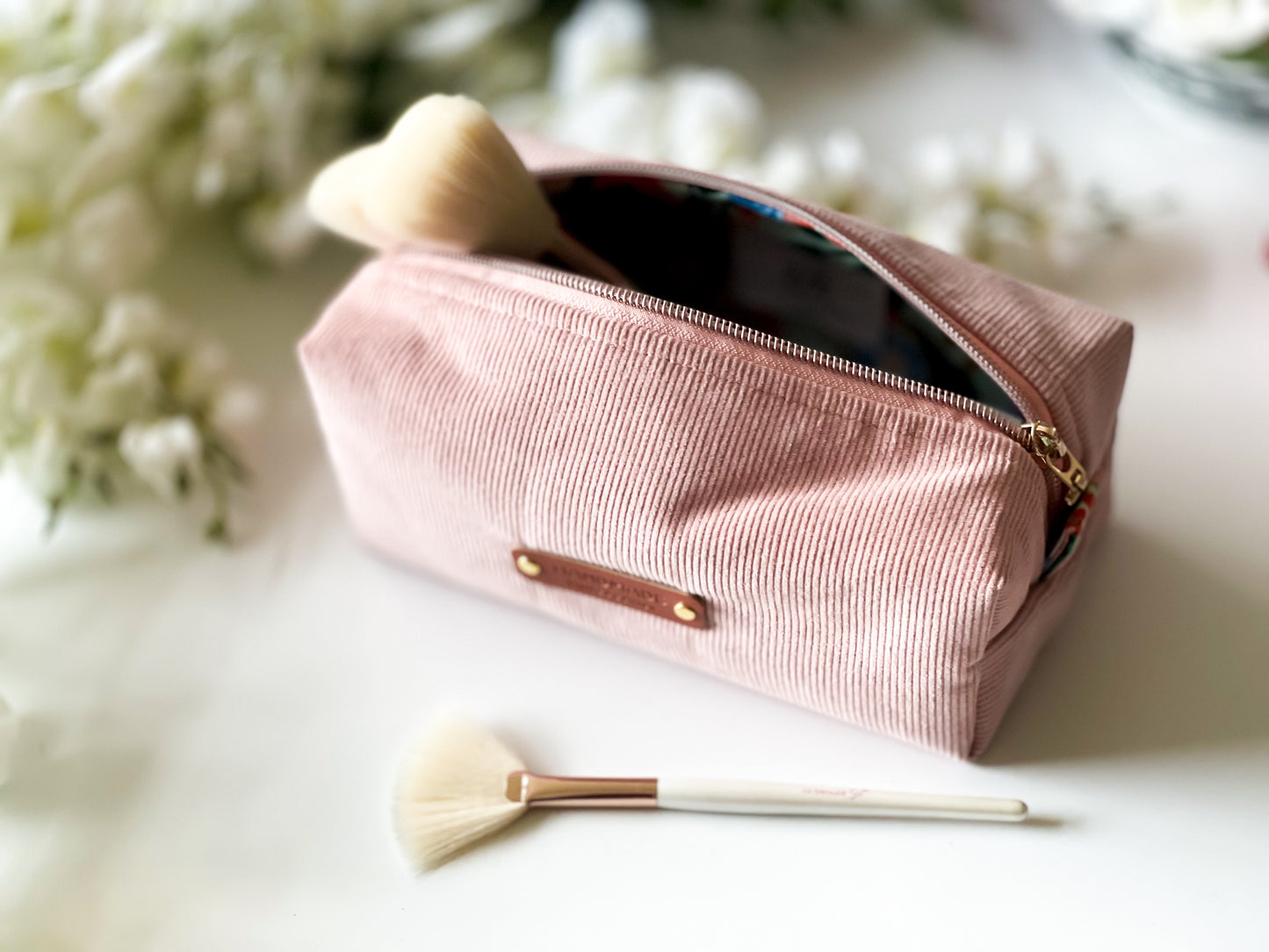 Pink makeup pouch with brushes on a light surface with flowers in the background