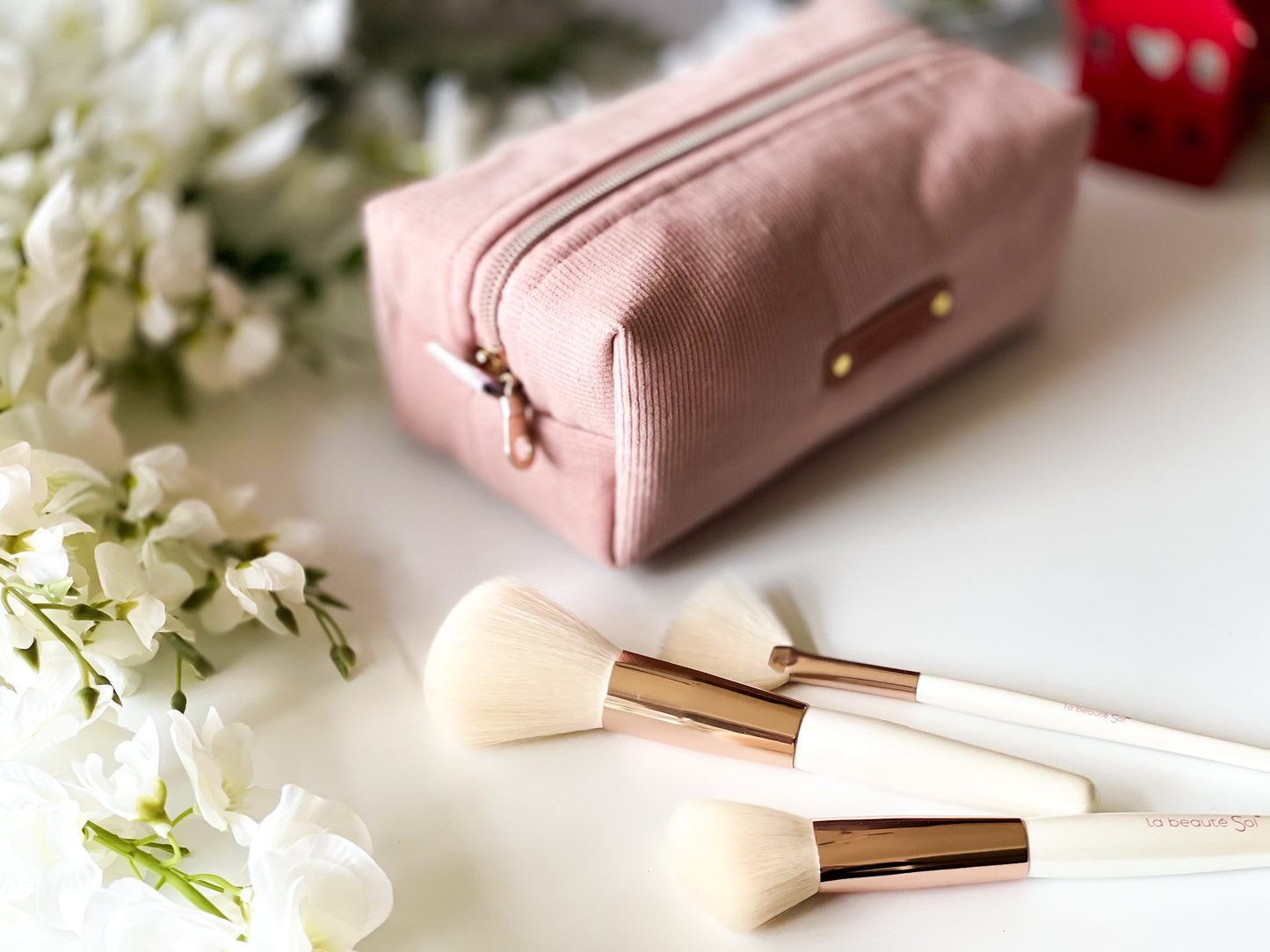 Pink makeup pouch with brushes on a white surface with flowers