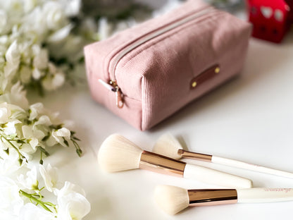 Pink makeup pouch with brushes on a white surface with flowers