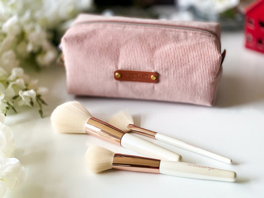 Makeup brushes with a pink pouch on a light surface with flowers in the background