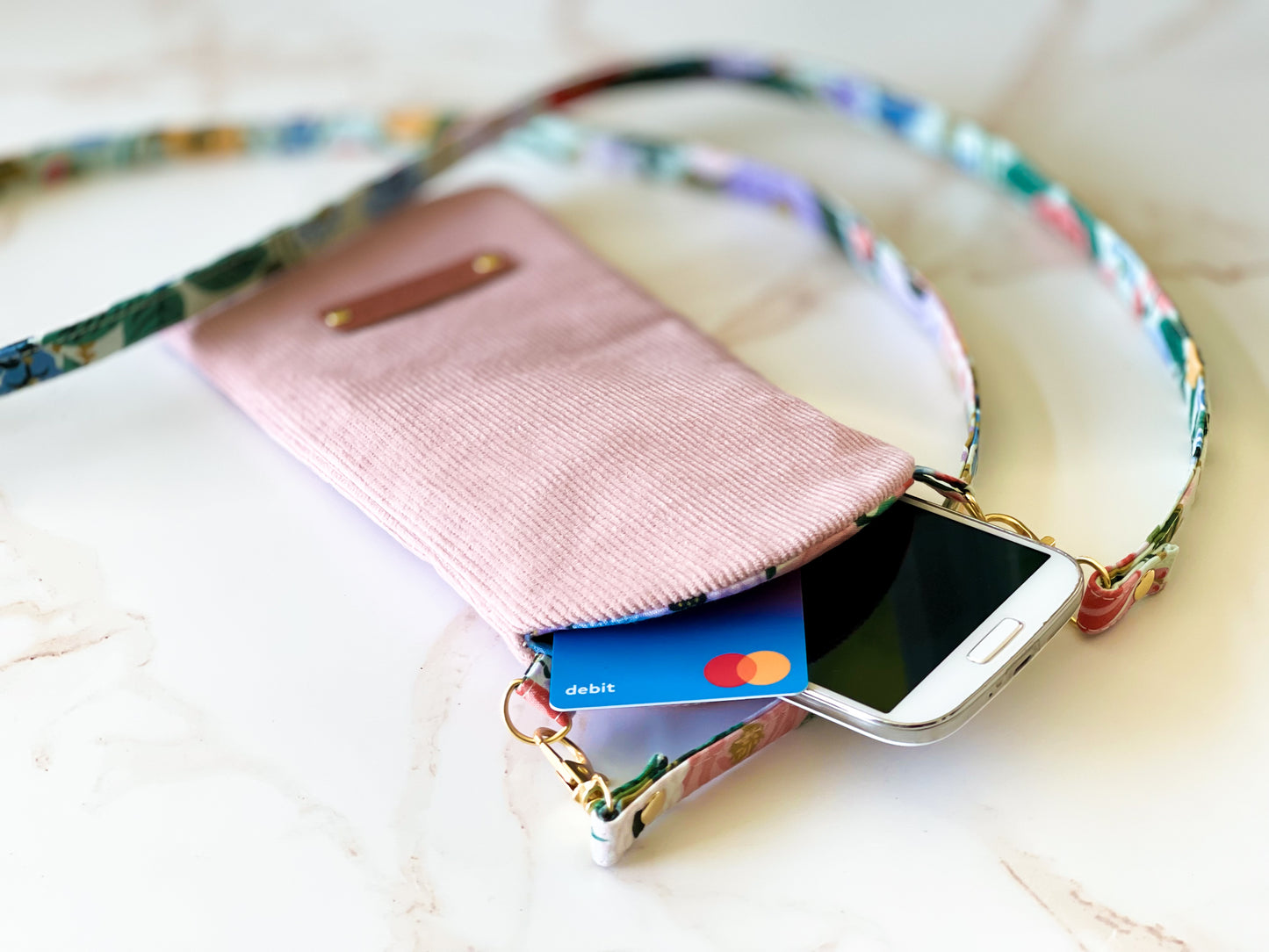 Pink phone case with floral strap holding a smartphone and card on a light background