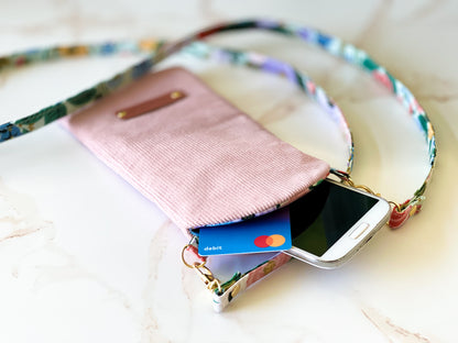 Pink phone case with floral strap holding a smartphone and card on a light background