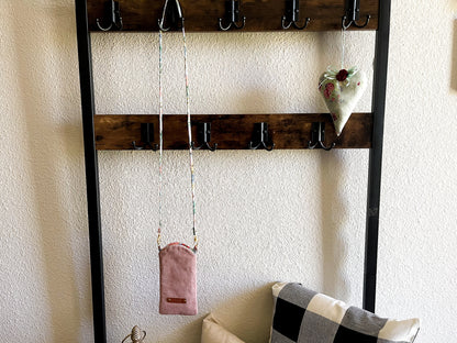 Wooden wall organizer with hooks holding a necklace, pouch, and decorative item against a white wall.