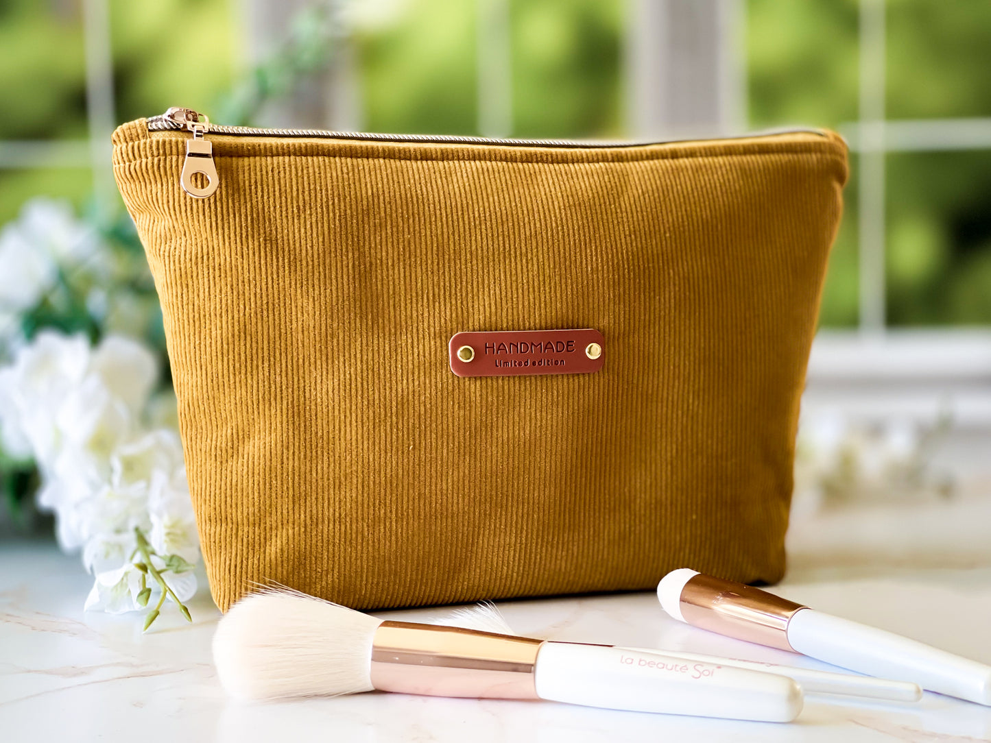 Mustard yellow makeup bag with 'Handmade' label on a white surface with makeup brushes.