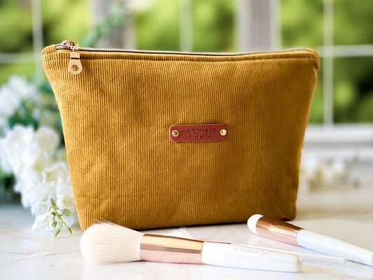 Mustard yellow makeup bag with 'Handmade' label on a white surface with makeup brushes.