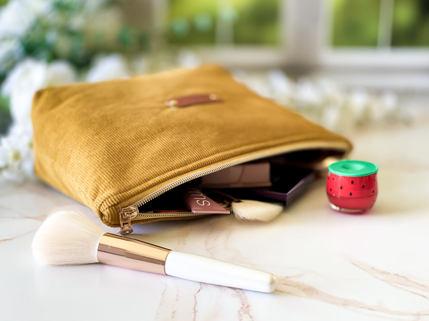 Yellow makeup pouch with cosmetic items and a brush on a light surface.