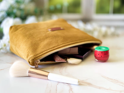 Yellow makeup pouch with cosmetic items and a brush on a light surface.