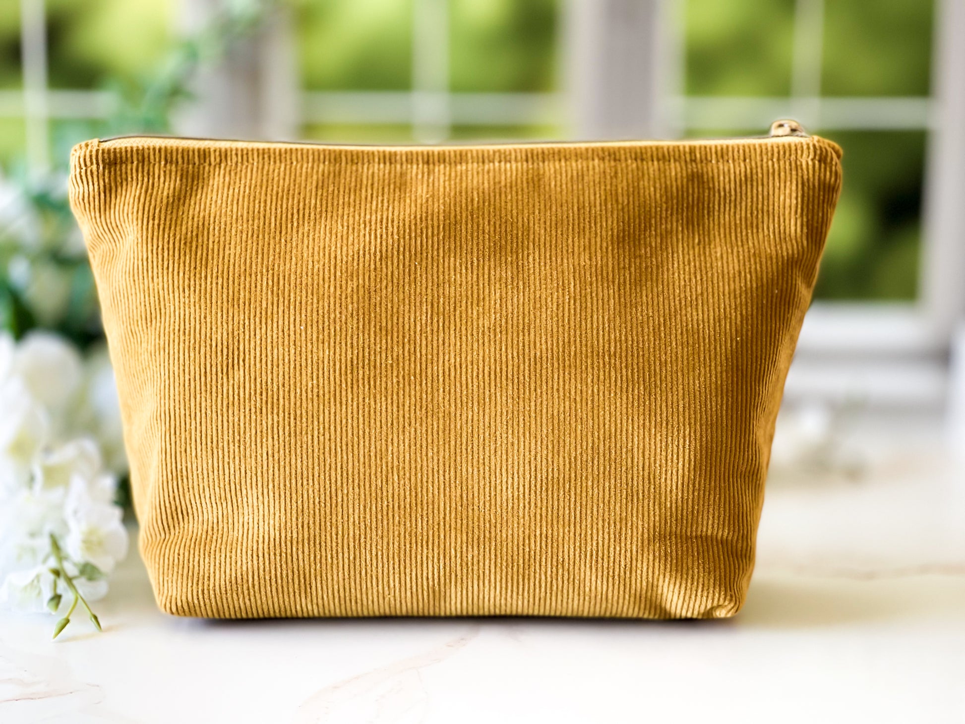 Gold corduroy pouch on a white surface with blurred greenery in the background
