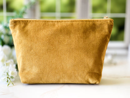 Gold corduroy pouch on a white surface with blurred greenery in the background