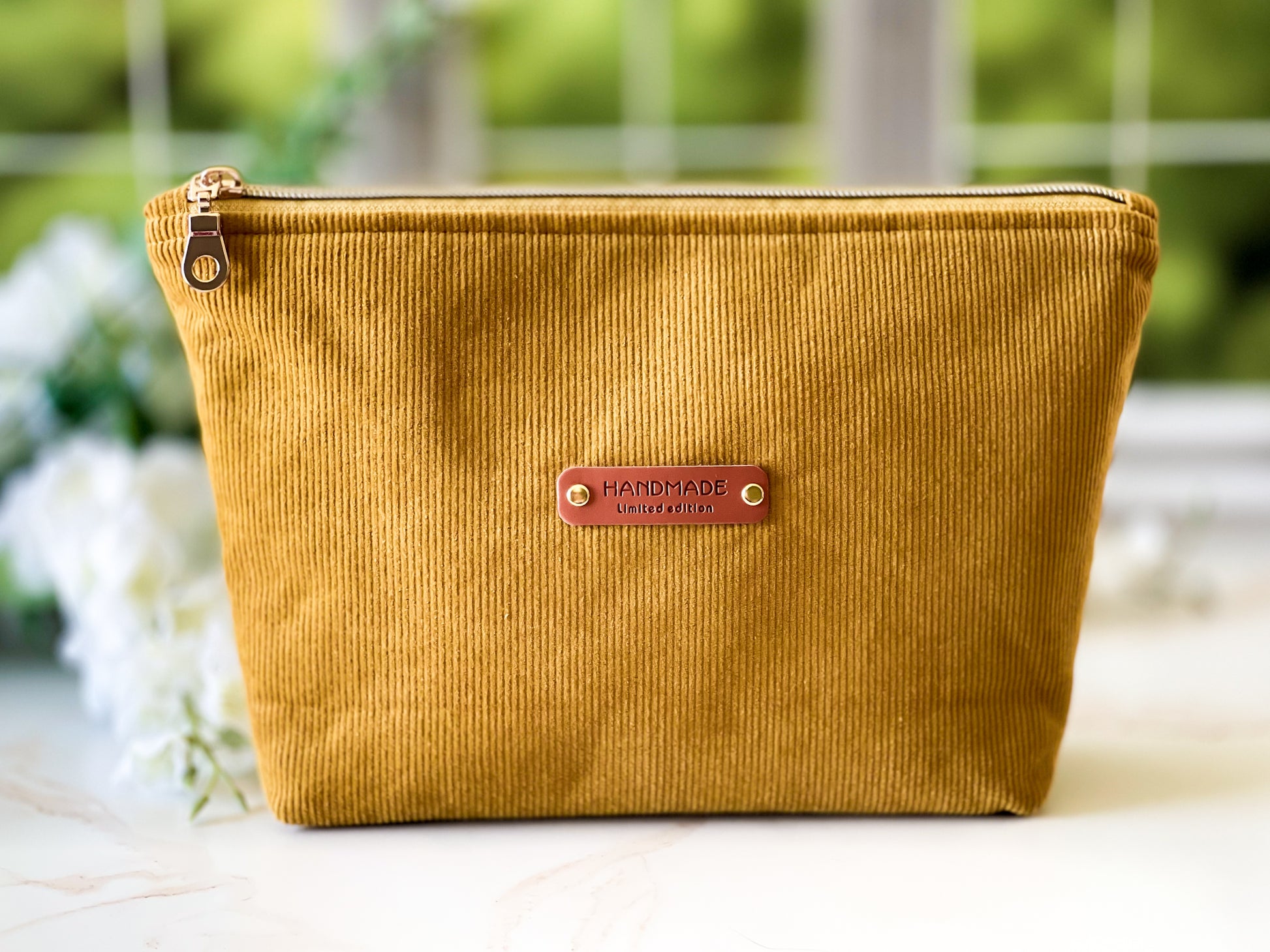 Yellow corduroy pouch with a 'Handmade' label on a blurred natural background