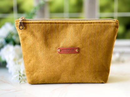 Yellow corduroy pouch with a 'Handmade' label on a blurred natural background