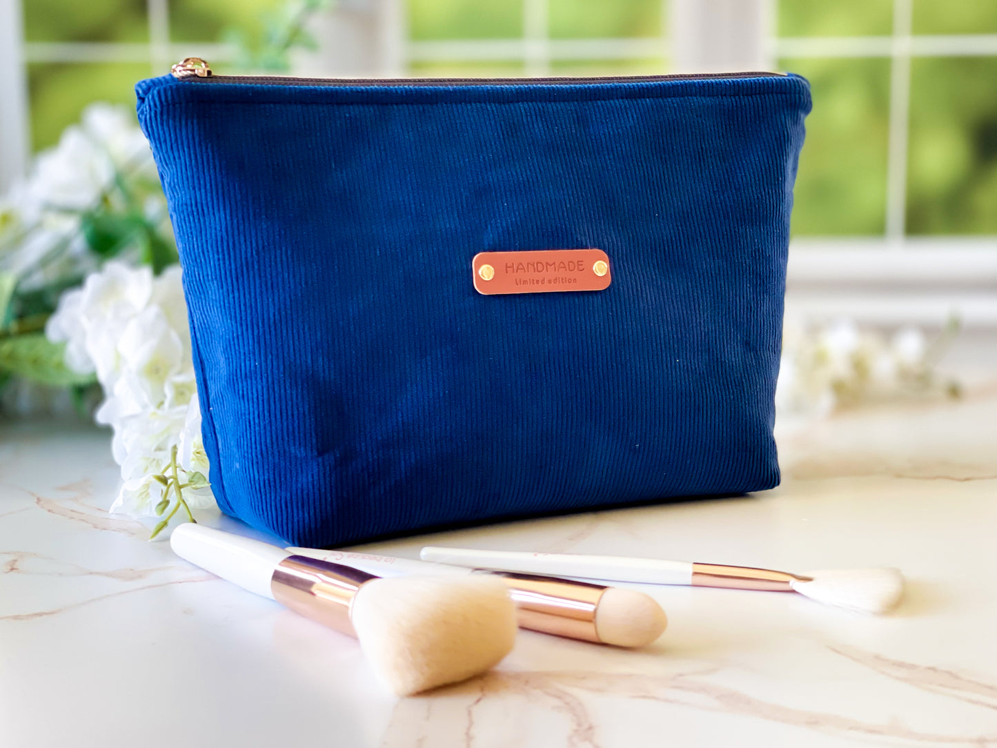 Navy Corduroy Cosmetic Bag - Blue makeup pouch with a brown label on a light surface with makeup brushes.