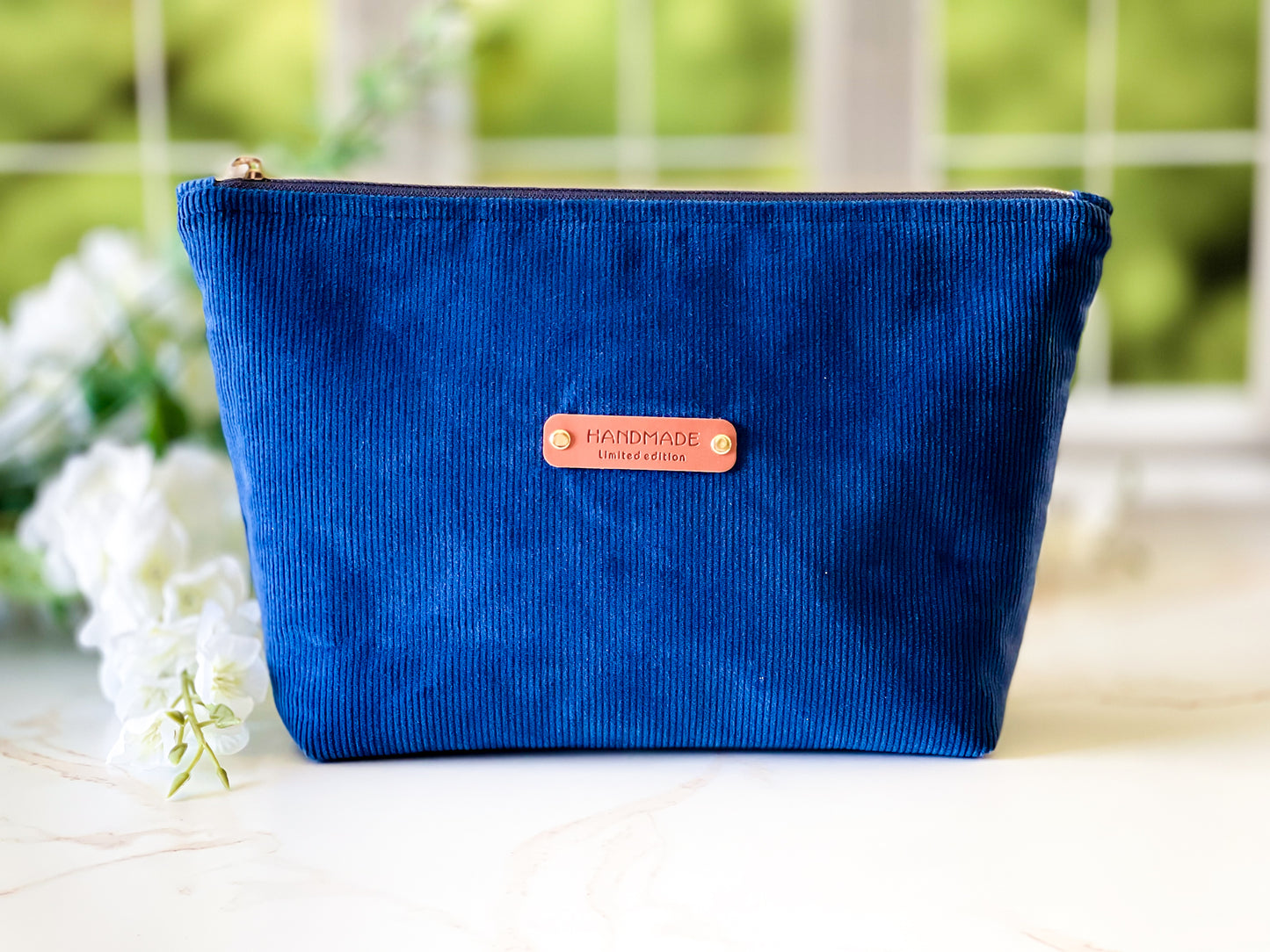 Navy Corduroy Cosmetic Bag - Blue corduroy pouch with a 'handmade' label on a blurred natural background