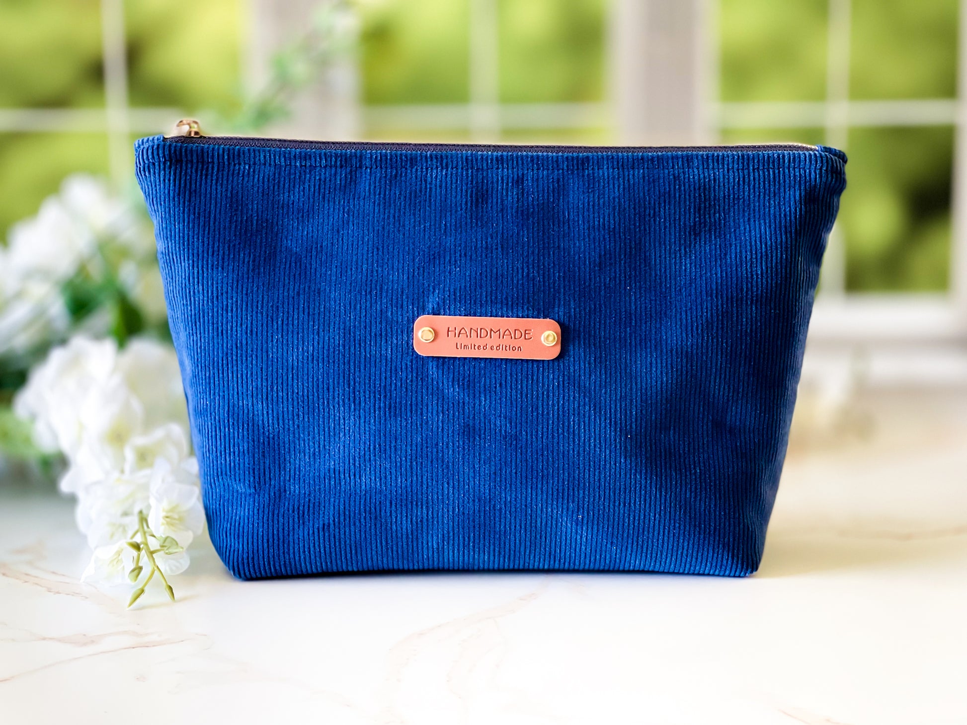 Navy Corduroy Cosmetic Bag - Blue corduroy pouch with a 'handmade' label on a blurred natural background