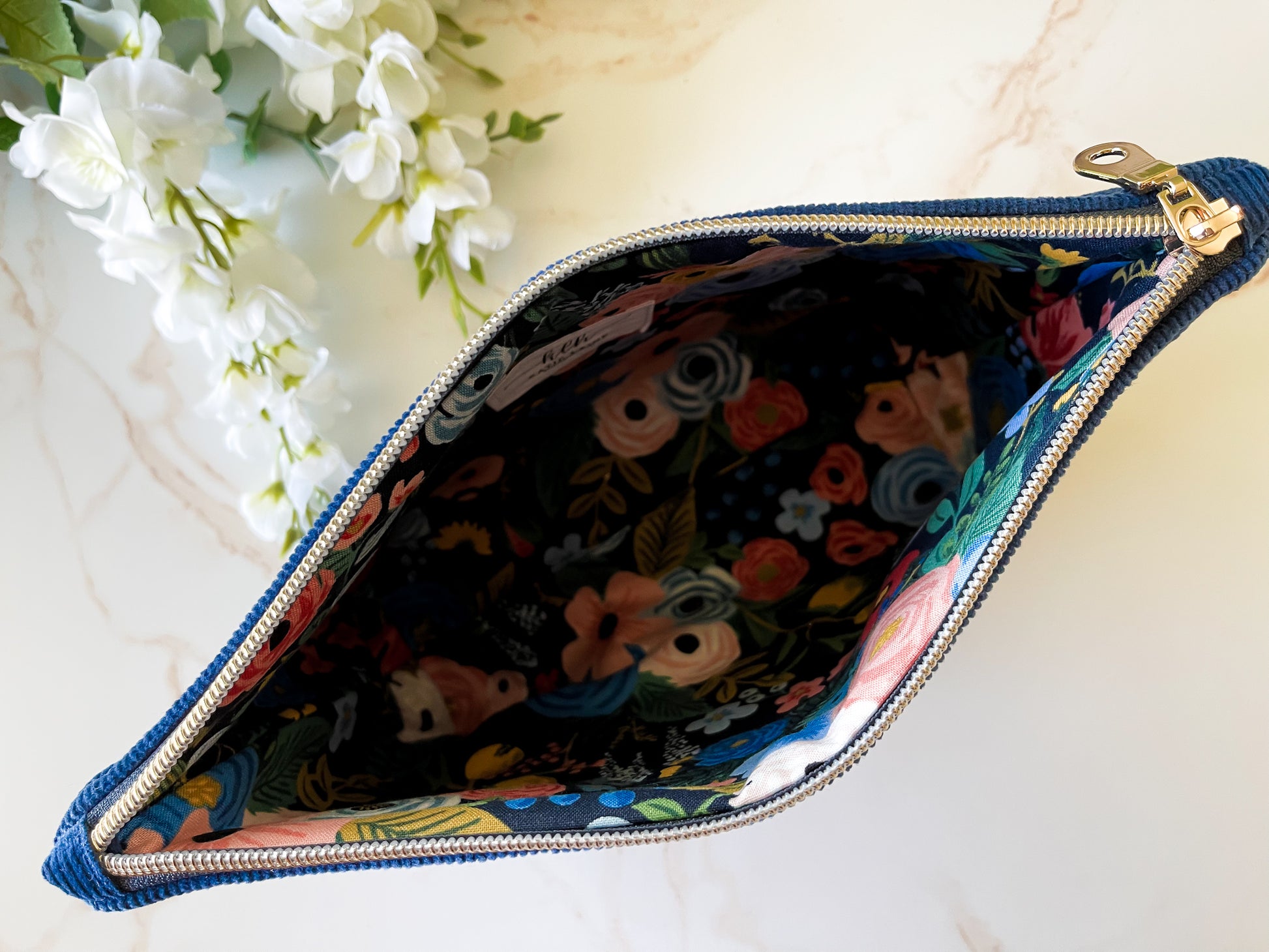 Navy Corduroy Cosmetic Bag - Open Zipped pouch with colorful interior design on a marble surface with flowers.