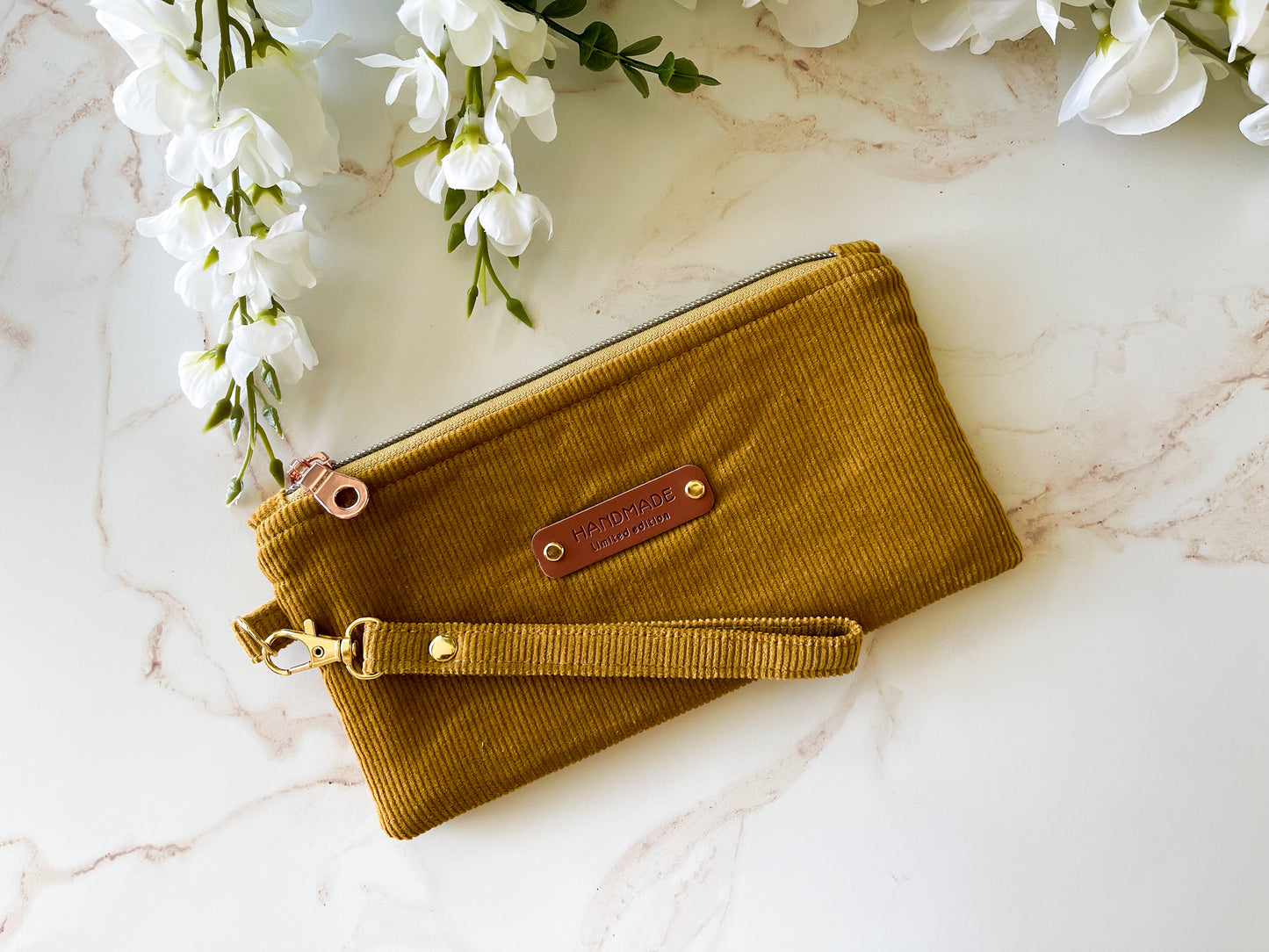 Brown clutch bag with strap on a marble surface with white flowers