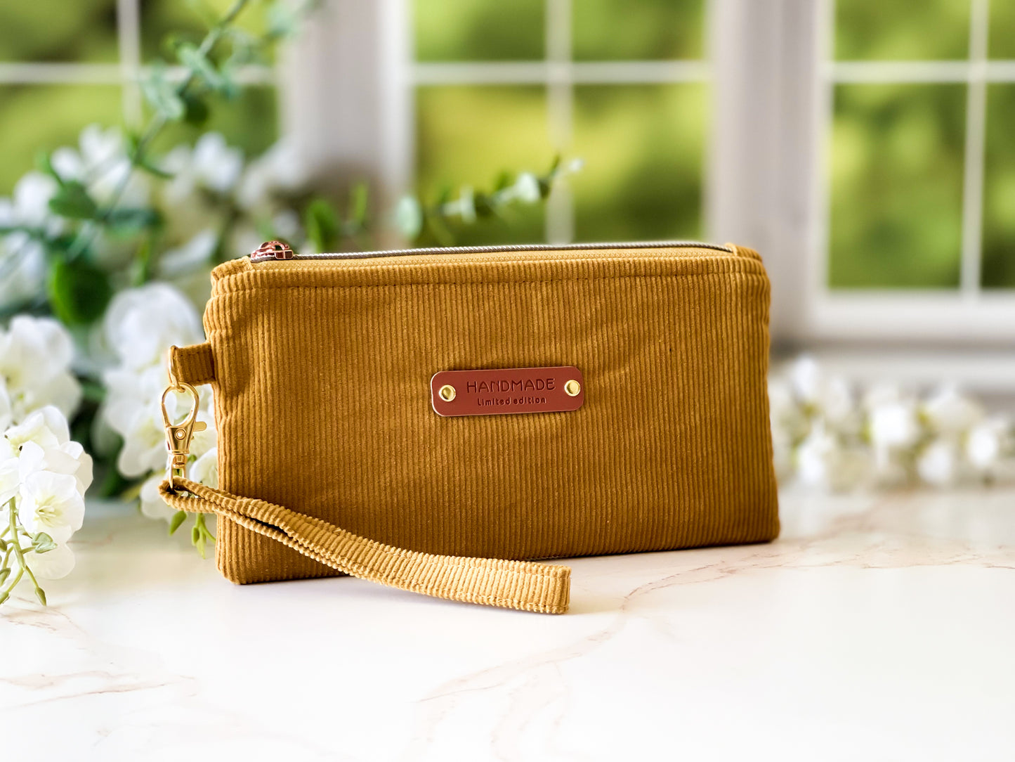 Yellow clutch bag with a brand label on a light surface with blurred greenery in the background