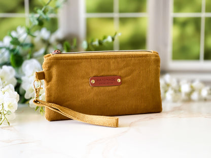 Yellow clutch bag with a brand label on a light surface with blurred greenery in the background