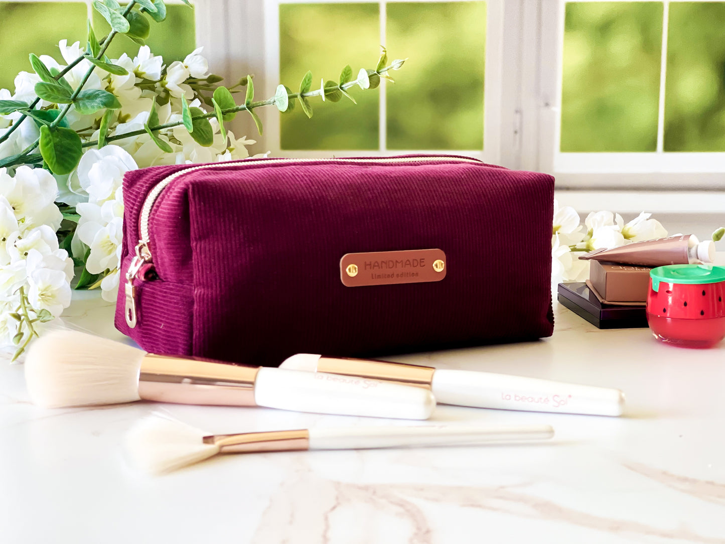 Merlot Corduroy Boxy Bag - Maroon cosmetic bag with makeup brushes on a table with a window in the background