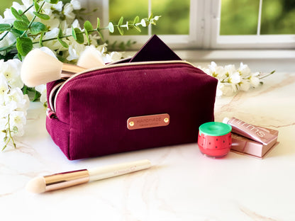 Merlot Corduroy Boxy Bag - Maroon cosmetic bag with makeup items on a light surface with flowers in the background